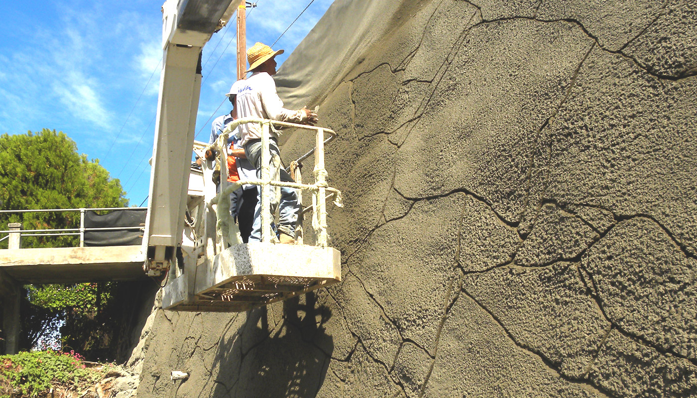 Photo: worker in lift applying texture detail to the faux stone shotcrete retaining wall