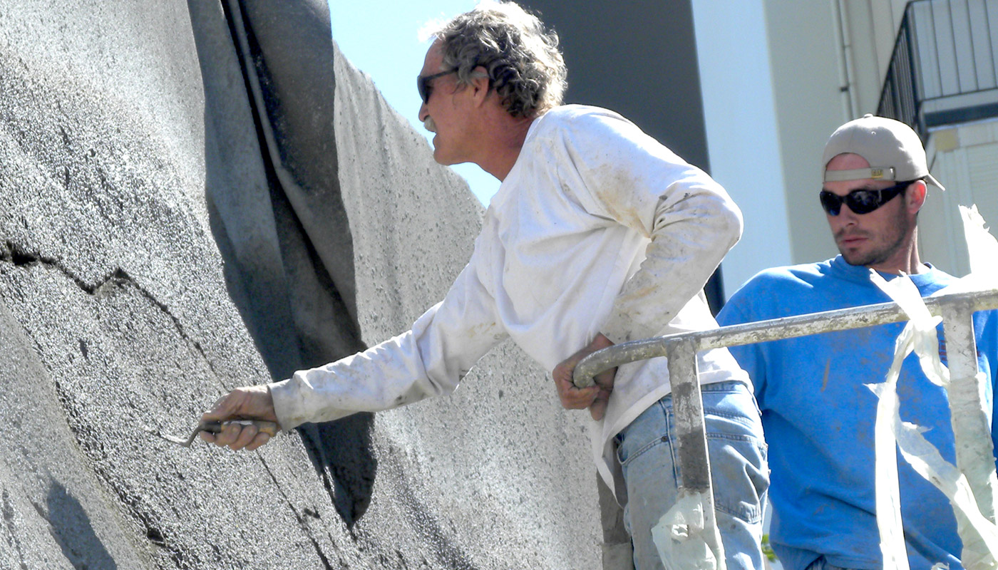 Photo: Workers in a lift applying texture and color effects to the shotcrete retaining wall